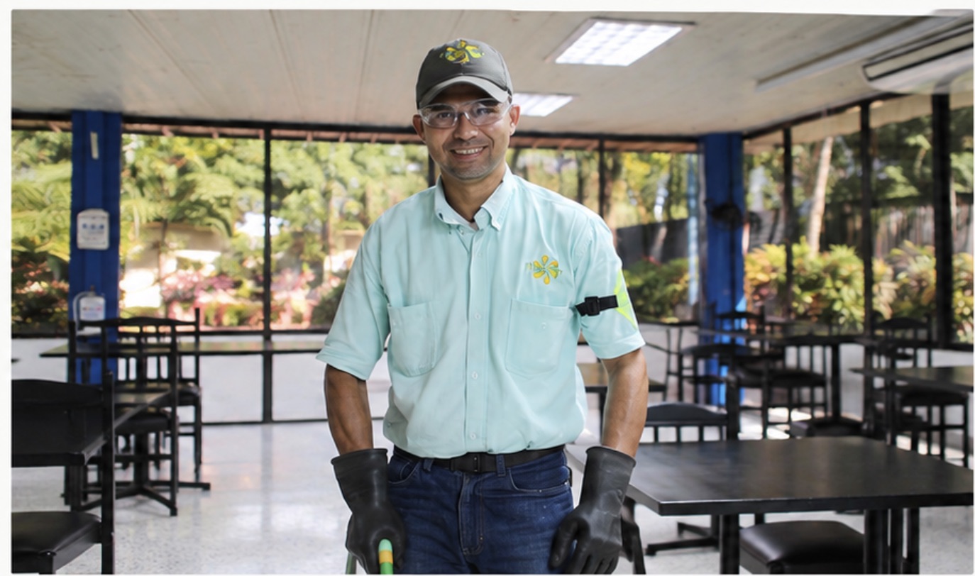Colaborador de Florecer uniformado, con gorra, gafas y guantes de protección en una cafetería empresarial